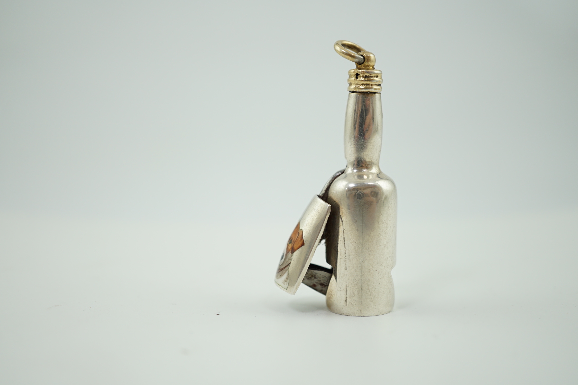 A late Victorian novelty parcel gilt silver cigar cutter, modelled as a bottle, the hinged section enamelled with a head of a dog